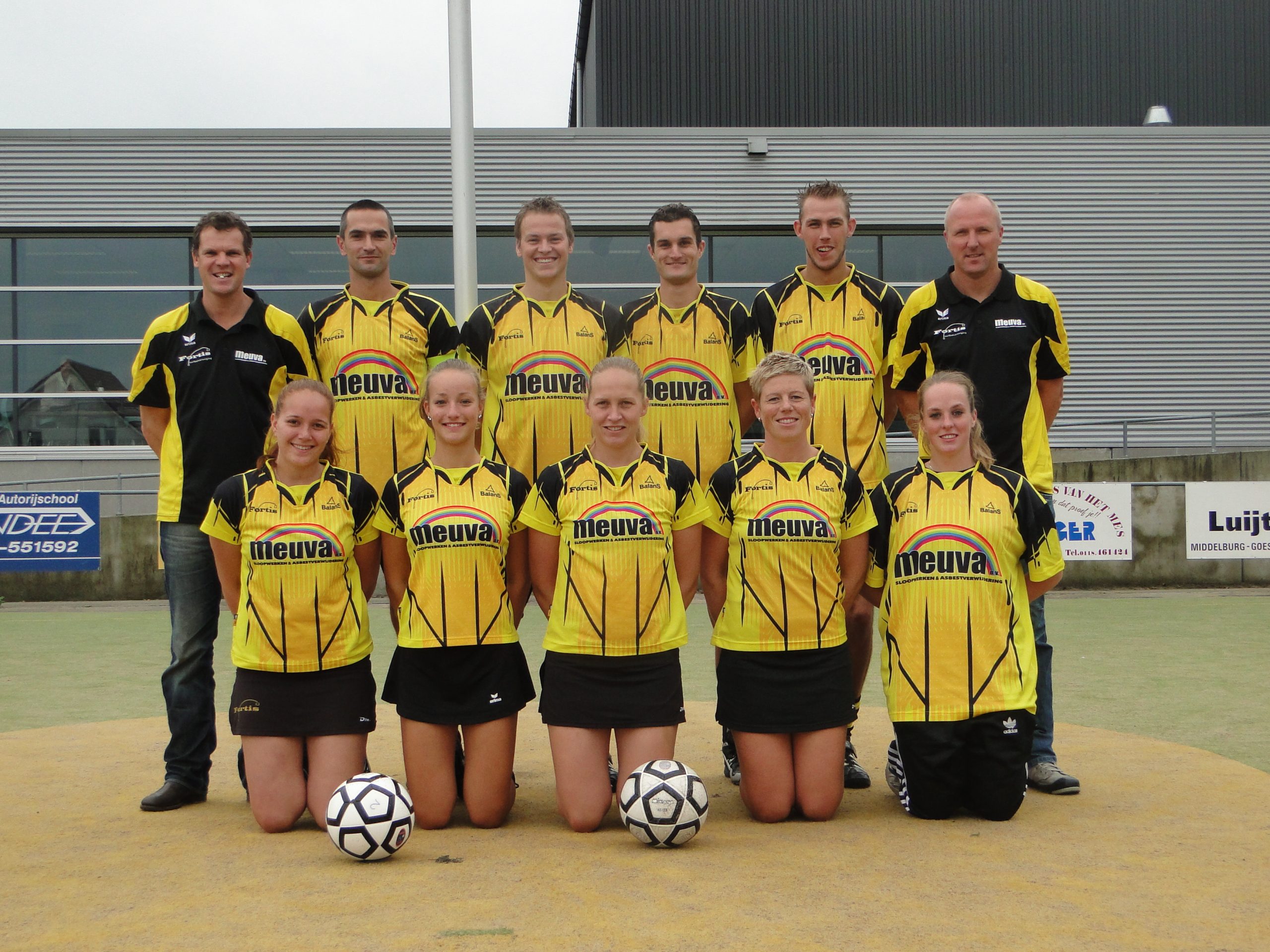 Een gemengd Fortis-team poseert in geel-zwarte shirts voor het clubgebouw.